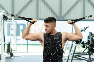 Genç bir adam modern bir spor salonunda biseptik kablo egzersizi yapıyor..