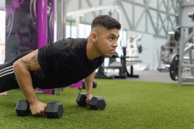 Kararlı bir adam modern bir spor salonunda yapay sahada dambıl şınav çeker..