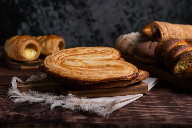 Kırsal bir ahşap masa, palmiyeler, kremalı börekler ve diğer lezzetli tatlılar da dahil olmak üzere çeşitli yeni pişmiş hamur işleri sergiler..