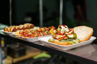 Close-up of a freshly prepared burger, garnished with various toppings, resting on a disposable white tray.