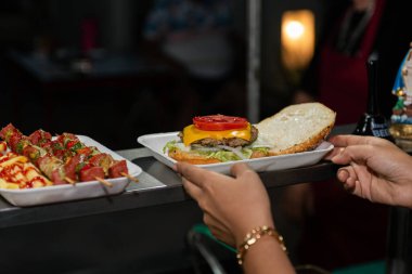 Close-up of a freshly prepared burger, garnished with various toppings, resting on a disposable white tray.