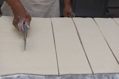 Bir fırıncının elleri hamur yaprağını ustalıkla dilimler hatta bir hamur bıçağı kullanarak şeritlere ayırır..