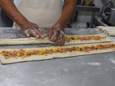 Bir fırıncı dikkatlice içi doğranmış jambon, peynir ve biberle dolu hamur işleri yapar..