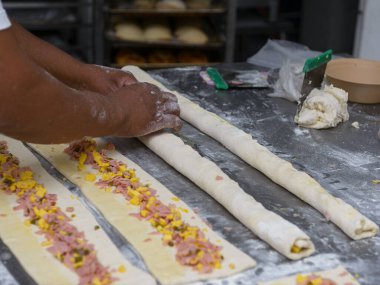 Bir fırıncı dikkatlice içi doğranmış jambon, peynir ve biberle dolu hamur işleri yapar..