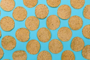 Açık mavi-yeşil arkaplanda dikkatlice dizilmiş sayısız yuvarlak nachos..