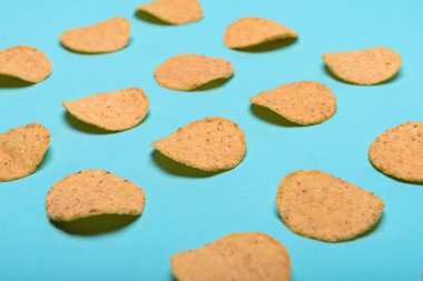 Açık mavi-yeşil arkaplanda dikkatlice dizilmiş sayısız yuvarlak nachos..