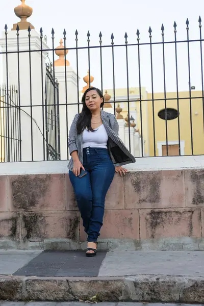 Genç bir kadın tesadüfen alçak bir duvarda oturuyor, yıpranmış taş duvarlar ve arka planda işlenmiş demir çitler..