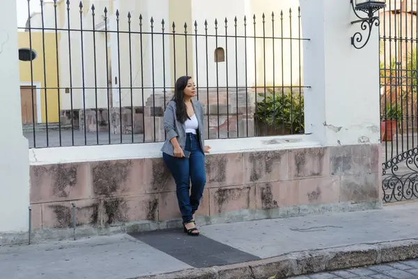 Genç bir kadın tesadüfen alçak bir duvarda oturuyor, yıpranmış taş duvarlar ve arka planda işlenmiş demir çitler..