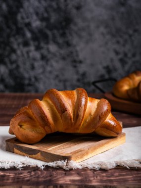 İki yeni pişmiş kruvasan, altın rengi kahverengi ve pırıl pırıl, ahşap bir tahtanın üzerinde keten bir kumaşın üzerinde dinleniyor..