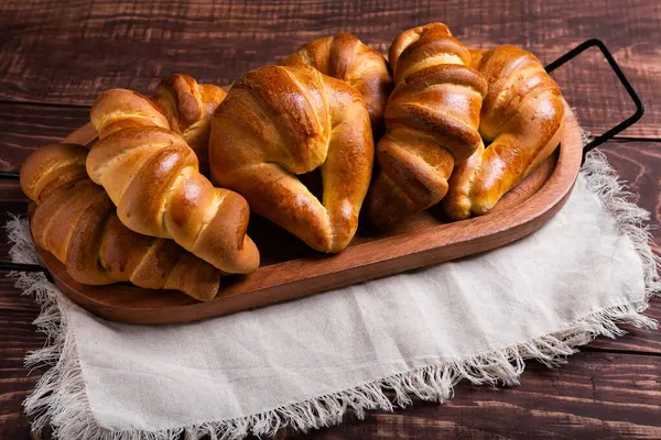 Ahşap tepside taze pişmiş ekmek ruloları ve kruvasanlardan oluşan bir karışım bulunur..