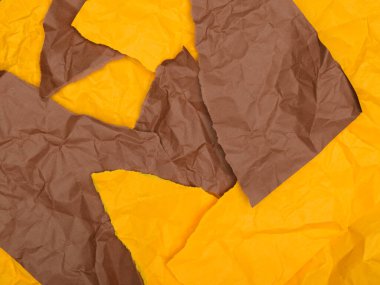Buruşuk kahverengi ve sarı kağıt parçaları, desenli, soyut bir arkaplan oluşturuyor..