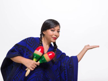 Canlı mavi bir panço giyen bir kadın bir çift marakas tutuyor ve bir şey tutuyor gibi elini uzatıyor..