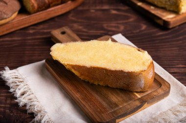 Lezzetli bir dilim tereyağlı tatlı ekmek, kahverengileşmiş ve cömertçe şekerle kaplanmış, kırsal bir tahtanın üzerinde duruyor..