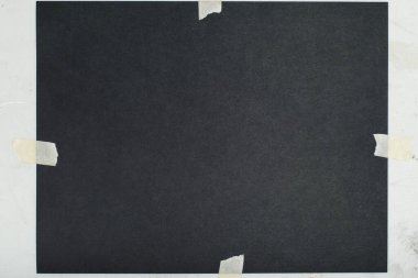 Koyu kare bir kağıt parçası, muhtemelen kağıt parçası, daha hafif bir arka plana bantlanmış.