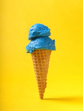 İki kepçe parlak mavi sakızlı dondurma gevrek bir waffle külahının üzerinde oturur, güneşli sarı bir arka fonda..