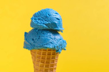 İki kepçe parlak mavi sakızlı dondurma gevrek bir waffle külahının üzerinde oturur, güneşli sarı bir arka fonda..