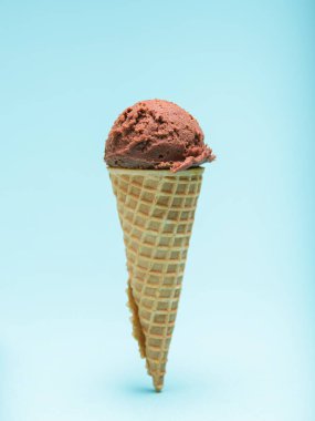 Kıtır bir waffle külahının tepesinde açık mavi bir arka planda bir kepçe zengin çikolatalı dondurma..