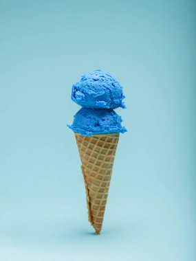 Çift kepçe canlı mavi dondurma gevrek bir waffle konisi üzerinde oturur, yumuşak açık mavi bir arka planda..