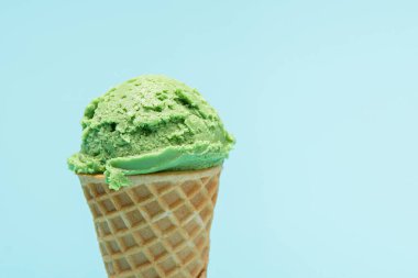 Kıtır waffle külahının tepesinde açık mavi bir arka planda canlı yeşil naneli dondurma kepçesi..
