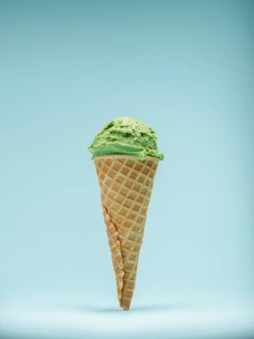 Kıtır waffle külahının tepesinde açık mavi bir arka planda canlı yeşil naneli dondurma kepçesi..