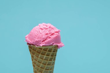 İki kepçe canlı pembe dondurma gevrek bir waffle külahının üstünde, açık mavi bir arka fonda..