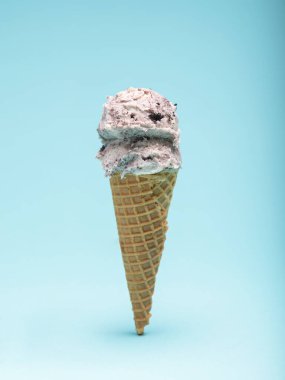Çıtır waffle külahının tepesinde açık mavi bir arka planda bir kepçe kurabiye ve dondurma..