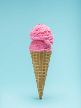 İki kepçe canlı pembe dondurma gevrek bir waffle külahının üstünde, açık mavi bir arka fonda..