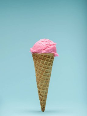 İki kepçe canlı pembe dondurma gevrek bir waffle külahının üstünde, açık mavi bir arka fonda..