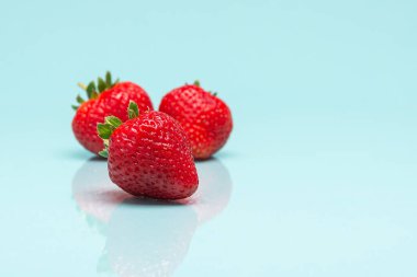 Üç olgun çilek açık mavi bir yüzeyde dinleniyor, biri diğerlerinden biraz farklı..