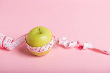 Pembe bir bant ile çevrili yeşil bir elma pembe bir arka planda duruyor..