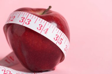 Kırmızı elma ve pembe arka planda pembe bir mezura, sağlıklı beslenme ve kilo yönetimi.