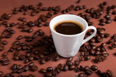 Yansıtıcı yüzeyde kavrulmuş fasulyelerle çevrili koyu kahveyle dolu bir espresso bardağı..