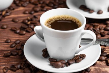 Kahverengi ahşap bir yüzey üzerinde kahve çekirdekleri ile çevrili, beyaz bir fincan üzerinde koyu kavrulmuş bir kahve.