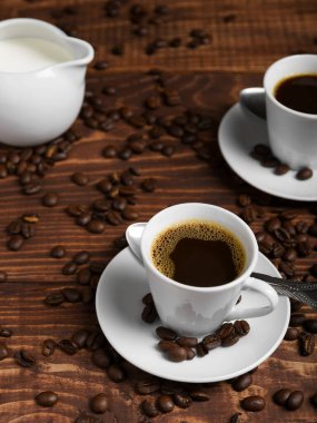 İki espresso fincanı ahşap bir masanın üzerinde koyu kahve ile dolu, dağınık kahve çekirdekleri ile çevrili..