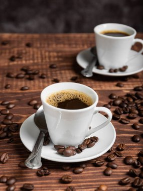 İki espresso fincanı ahşap bir masanın üzerinde koyu kahve ile dolu, dağınık kahve çekirdekleri ile çevrili..