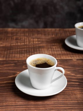 İki beyaz fincan koyu kahve zengin bir kahverengi ahşap masada oturur..