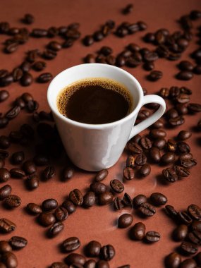 Yansıtıcı yüzeyde kavrulmuş fasulyelerle çevrili koyu kahveyle dolu bir espresso bardağı..