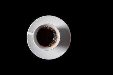 Dumanı tüten koyu bir kahve fincanı, siyah bir fonda beyaz bir fincan üzerinde oturur..