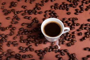 Yansıtıcı yüzeyde kavrulmuş fasulyelerle çevrili koyu kahveyle dolu bir espresso bardağı..