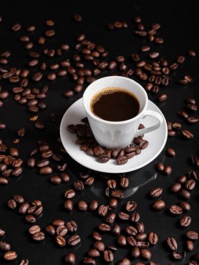 Yansıtıcı yüzeyde kavrulmuş fasulyelerle çevrili koyu kahveyle dolu bir espresso bardağı..