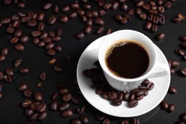 Yansıtıcı yüzeyde kavrulmuş fasulyelerle çevrili koyu kahveyle dolu bir espresso bardağı..