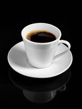 Dumanı tüten koyu bir kahve fincanı, siyah bir fonda beyaz bir fincan üzerinde oturur..