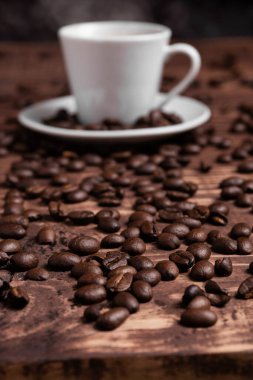 Kahve fincanına yakın, ahşap bir yüzeyde kavrulmuş kahve çekirdekleri..