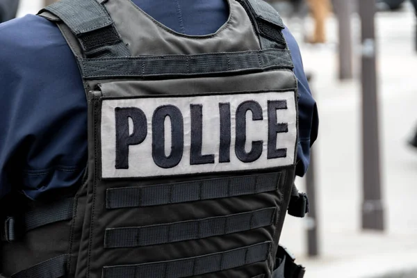 Single word \'POLICE\' marking written on the back of a bulletproof vest worn by a French police officer on a street in Paris, France. Concepts of law enforcement, crime, delinquency and criminal affairs