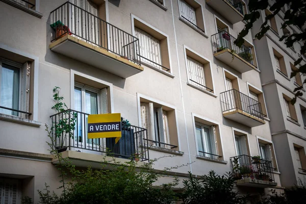 \'For Sale\' written in French on a yellow sign attached to the exterior of an apartment in a residential building. Concept of housing real estate market in France