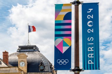 Paris, Fransa - 25 Temmuz 2024: Dikey pankartlar, Paris 2024 Yaz Olimpiyatları için renkli tabelalar, Fransa 'nın Paris şehrinde arka planda dalgalanan bir Fransız bayrağı