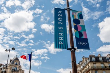 Paris, Fransa - 25 Temmuz 2024: Dikey pankartlar, Paris 2024 Yaz Olimpiyatları için arka planda Fransız bayrağı dalgalanan Paris, Fransa sokaklarında renkli tabelalar