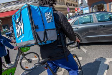 Paris, Fransa - 9 Nisan 2025: Delicity food dağıtım bisikleti sürücüsü Paris caddesinde trafikte. Delicity, Fransız fuar platformu. Restoran siparişi, teslimat ve rezervasyon için.