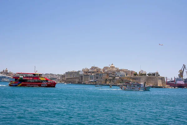 Valletta, Malta - 17 Haziran 2023: Valletta ile Vittoriosa arasındaki körfez, turistlerle geçen bir tekne ve gökyüzünde uluslararası bir uçak