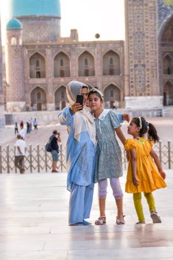 Semerkant, Özbekistan - 05 Temmuz 2024: Türbanlı Müslüman anne, Semerkant 'taki Registan Meydanı' nda kızlarıyla selfie çekiyor